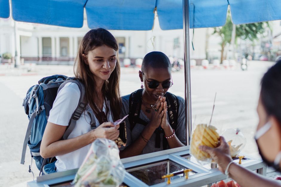 A close-up shot of various colorful and delicious street food items being sold at a bustling market, with a blurred person in the background enjoying the atmosphere.