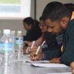 A group of diverse students and working adults collaborating and taking notes on laptops and tablets in a modern co-working space, demonstrating the various applications of note-taking apps.
