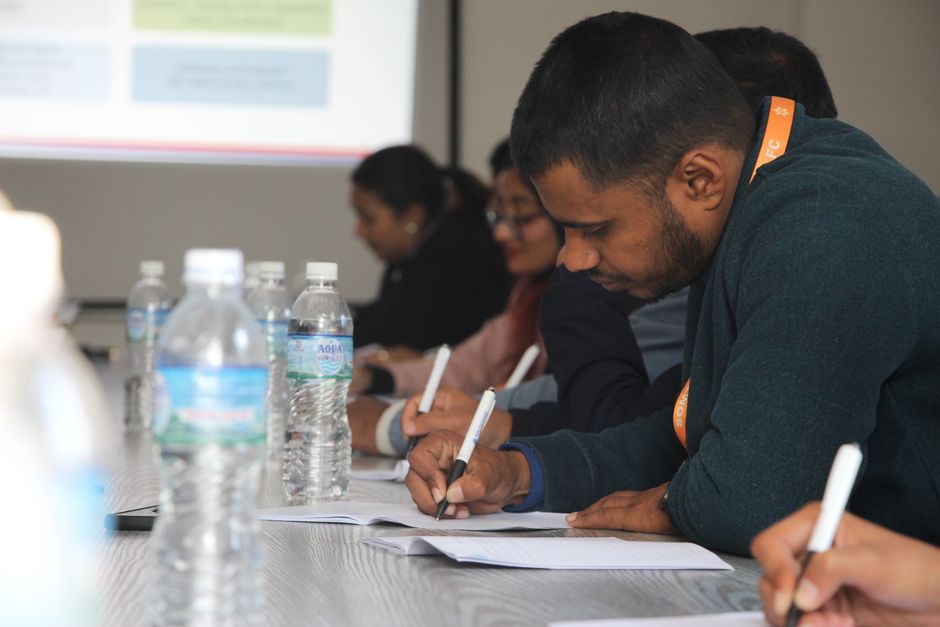 A group of diverse students and working adults collaborating and taking notes on laptops and tablets in a modern co-working space, demonstrating the various applications of note-taking apps.