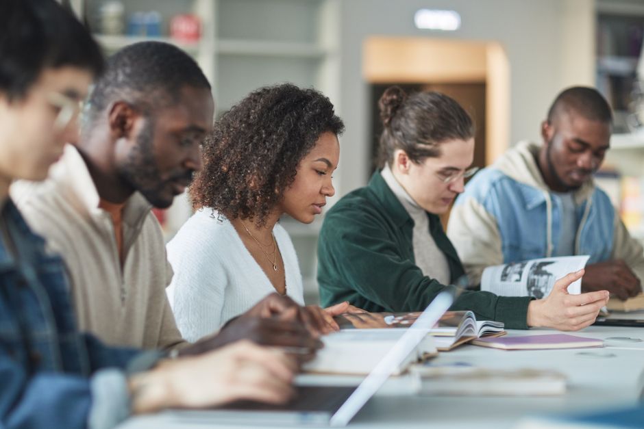 A diverse group of university students in a library setting, discussing research findings while one points to an AI-powered comparison on a tablet.