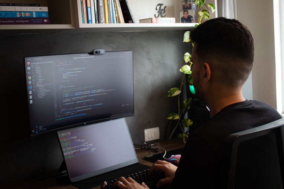 Close-up of a person using an ergonomic keyboard with an external monitor and a dedicated webcam in a bright home office setting.