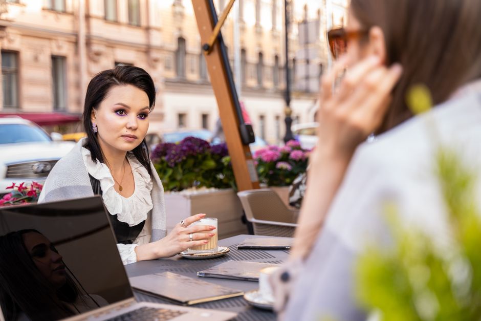 A person working on a laptop at an outdoor cafe in a charming European city square, with historic buildings in the background.