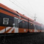 A sleek, modern high-speed train, possibly a TGV, speeding through a lush green European landscape under a clear sky.