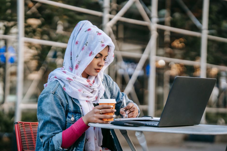 A person with a laptop at a cafe, surrounded by a travel journal and a smartphone, symbolizing an expat organizing their life.