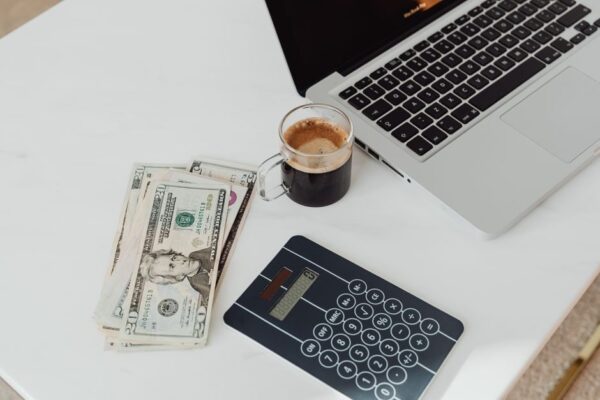 An expat woman with a laptop and coffee, reviewing her finances and a budget spreadsheet in a modern apartment.