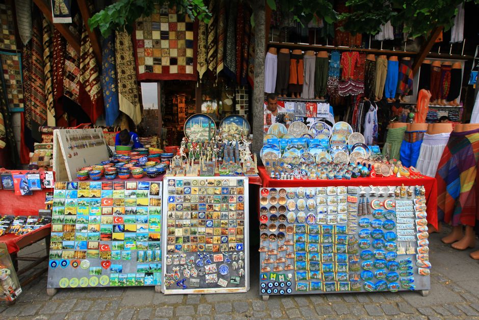 A person carefully arranging a small collection of travel souvenirs on a minimalist shelf, including a small ceramic bowl, a framed photo, and a unique stone, all thoughtfully spaced.