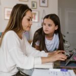 A family, including two parents and two children, sitting around a table with a laptop and smartphone, openly discussing digital boundaries and screen time rules.