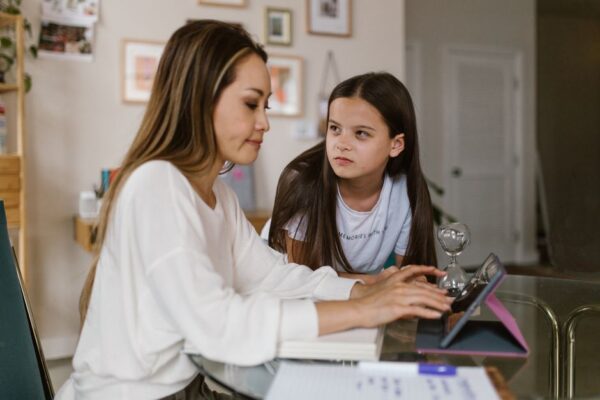 A family, including two parents and two children, sitting around a table with a laptop and smartphone, openly discussing digital boundaries and screen time rules.