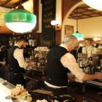 A budget-aware family of four, two adults and two children, enjoying small espressos and pastries while standing at a traditional counter in a bustling Roman coffee bar.