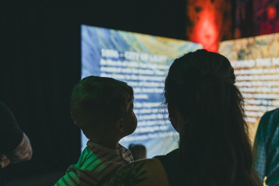 A family, including two children, looking intently at an interactive exhibit in a small, well-lit museum, demonstrating engaging cultural learning.