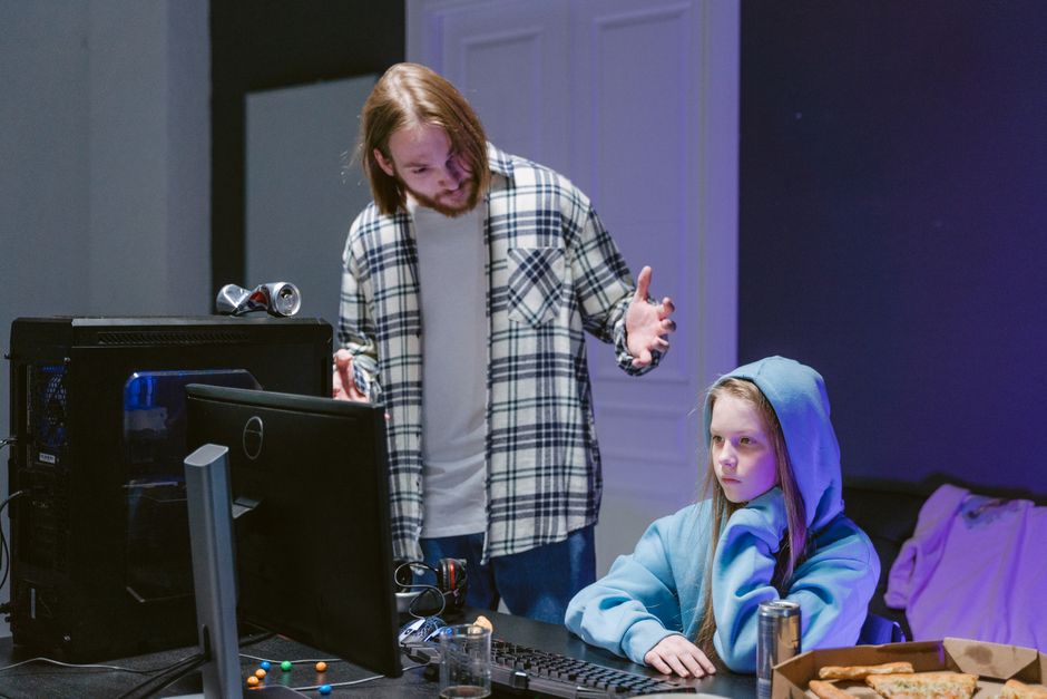 A parent and child happily playing a video game together on an older, non-gaming desktop PC.