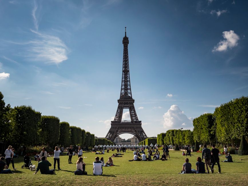 A family of four enjoying a relaxed picnic in a park in Paris, with the Eiffel Tower visible in the background, kids playing nearby.