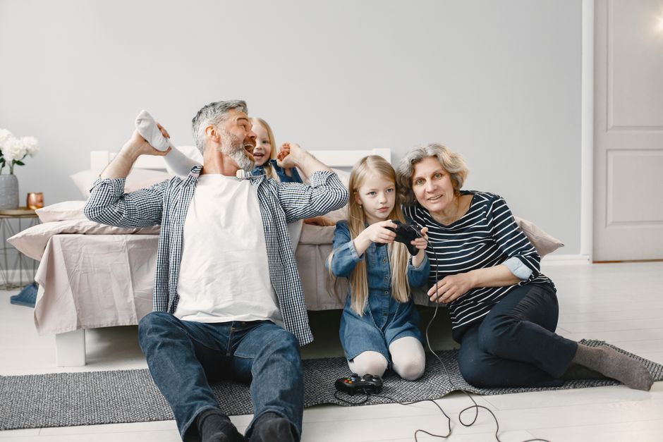 A family, including parents and children, gathered around a TV, smiling and playing a video game on a console.