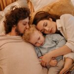 Family (parents and two young children) sleeping comfortably on a long-haul flight, one child nestled in a parent's lap, illustrating in-flight comfort for jet lag management.