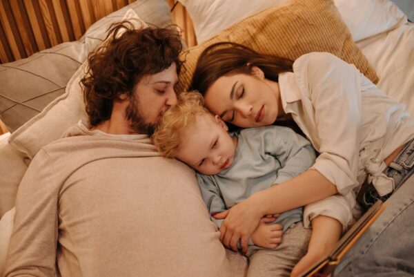Family (parents and two young children) sleeping comfortably on a long-haul flight, one child nestled in a parent's lap, illustrating in-flight comfort for jet lag management.