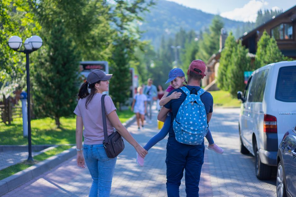 A parent and child looking at a phone screen displaying a pollen forecast while standing in front of a European landmark, suggesting preparation for seasonal allergies while traveling.
