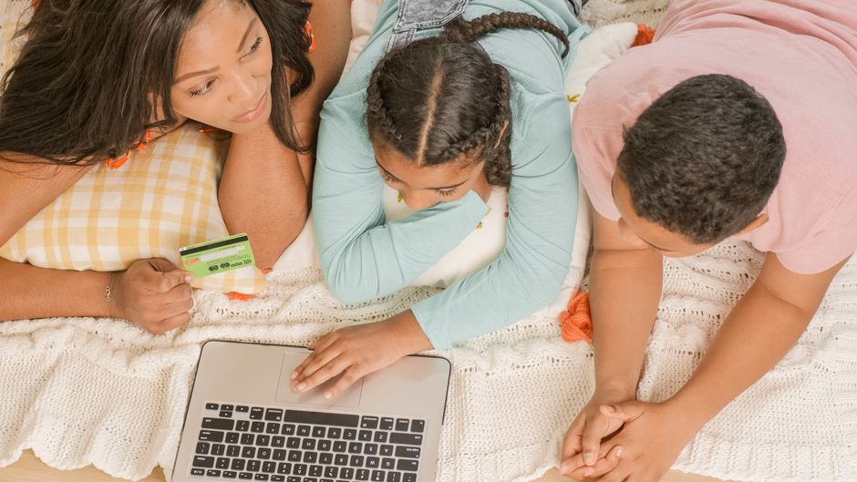 A diverse family of three, including parents and a child, sitting around a laptop, using it safely and collaboratively, representing digital security for families.