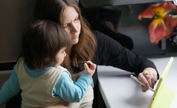 A family, including parents and children, gathered around a table with laptops, tablets, and phones, actively collaborating and using apps to organize their schedules and tasks.