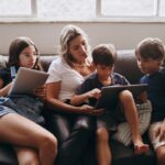A multi-generational family using various tech devices like laptops, tablets, and smartphones in a modern living room setting.