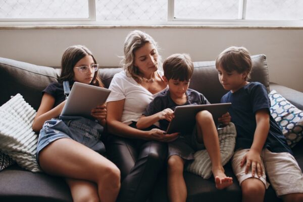 A multi-generational family using various tech devices like laptops, tablets, and smartphones in a modern living room setting.