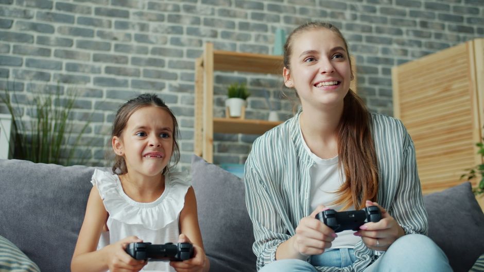 A parent and child on a video call with grandparents, all playing a colorful board game app together on their respective devices.