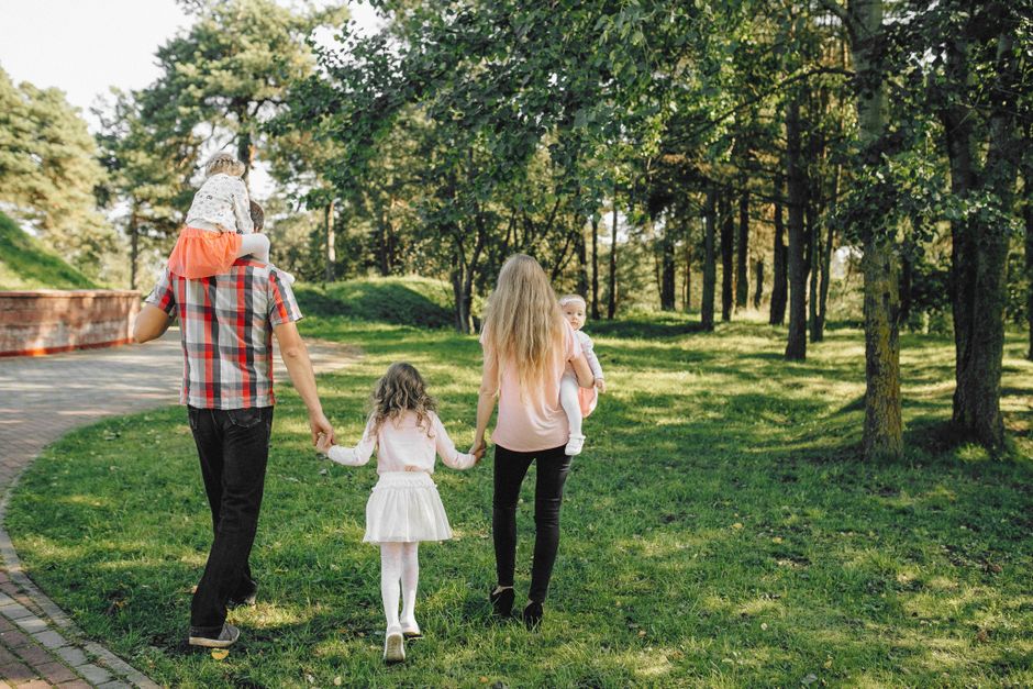 A family, including two parents and their children, enjoys a leisurely walk together in a sunny park.