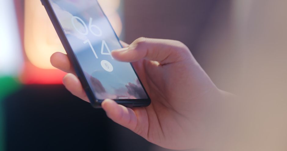 Close-up of a hand placing a thumb on a smartphone's fingerprint sensor, with a digital padlock icon superimposed on the screen.