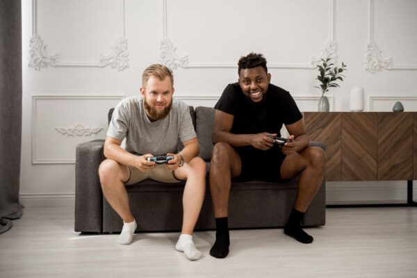 Friends using different gaming platforms (PlayStation, Xbox, PC) happily playing together on screens.