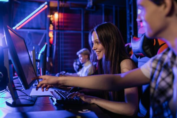 Three friends in different locations smiling and wearing headsets, each playing a video game on their individual screens, representing long-distance multiplayer.