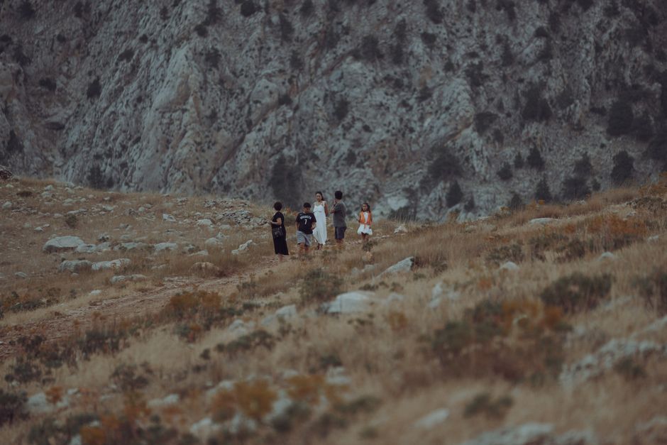 Three friends, two women and one man, smiling and looking at a scenic view while hiking on a mountain trail, representing shared outdoor activities.