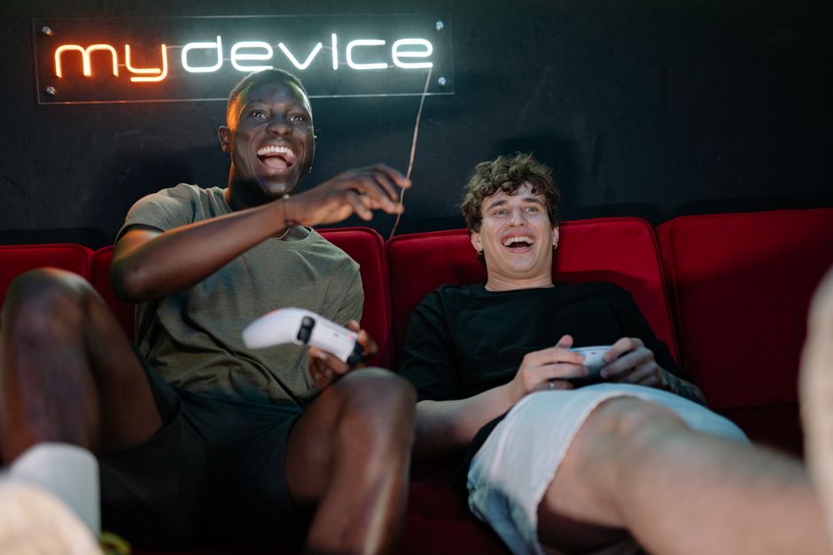 Three young adults gathered around a TV, laughing and playing a multiplayer video game on a Nintendo Switch, with foreign language text visible on screen.