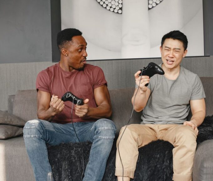 Two friends laughing while playing a local co-op game on a TV in a cozy living room, controllers in hand.