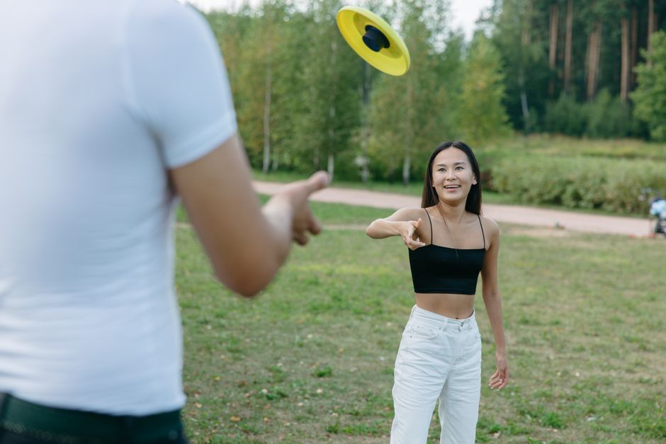 A group of friends laughing and playing frisbee in a sunny green park, with a cityscape in the distance.