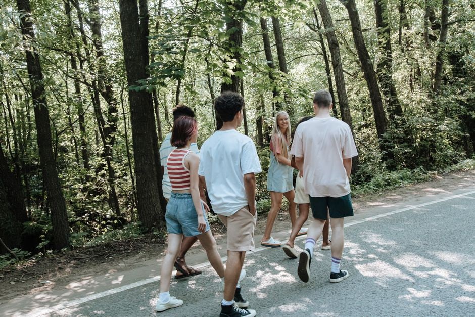 Two people laughing and walking together on a scenic trail lined with trees, suggesting a pleasant outdoor activity.