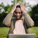 A person holding their head in frustration while looking at a buffering laptop screen, illustrating slow Wi-Fi problems.