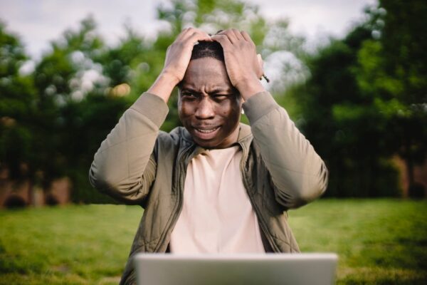 A person holding their head in frustration while looking at a buffering laptop screen, illustrating slow Wi-Fi problems.