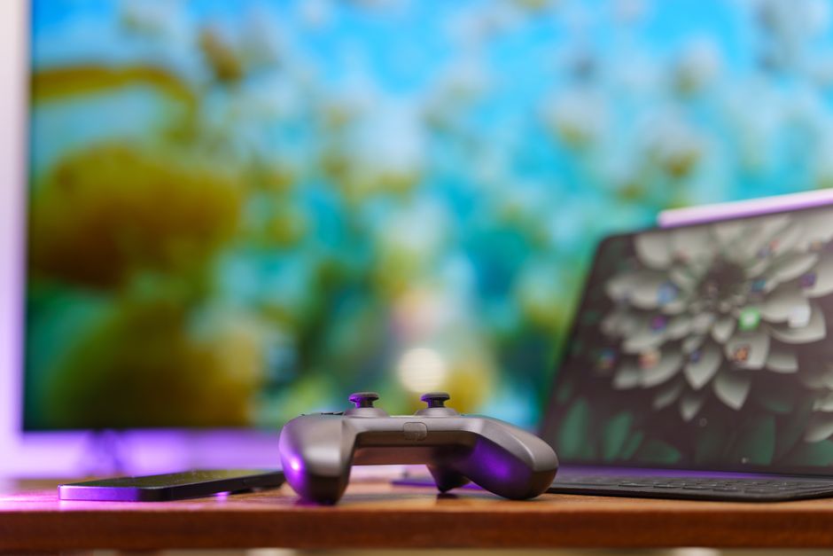 A modern Xbox controller resting on a wooden table, with a laptop in the background displaying the interface of a strategy game, illustrating console-friendly strategy options.