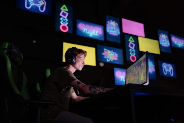 A person sitting on a couch, looking at a stack of game cases on one side and a console's digital store interface on a TV on the other, symbolizing the choice between digital and physical games.