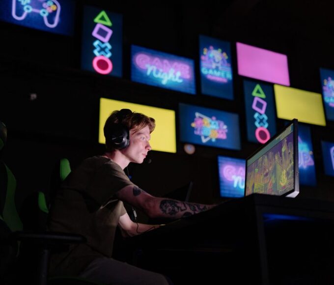 A person sitting on a couch, looking at a stack of game cases on one side and a console's digital store interface on a TV on the other, symbolizing the choice between digital and physical games.