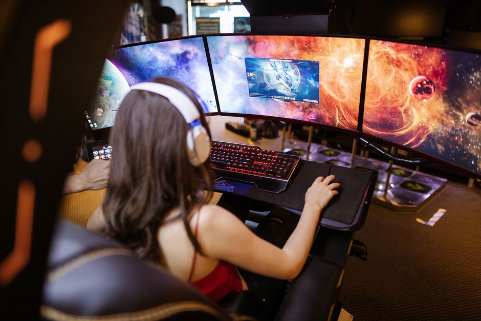 A person playing a video game on a large, high-refresh-rate curved monitor, showing vibrant in-game graphics and a gaming keyboard.