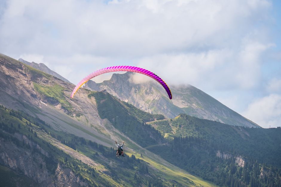 A character from Genshin Impact gracefully gliding over a lush, mountainous landscape, highlighting the game's expansive exploration.