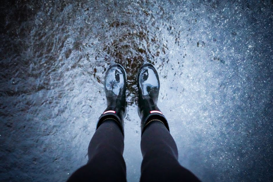 Close-up of sleek, waterproof GORE-TEX ankle boots stepping confidently through a puddle on a wet sidewalk.