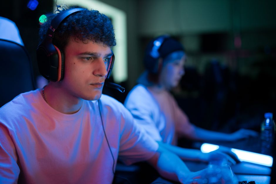 A close-up of a gaming headset with a blurred background of a screen and hands on a controller, symbolizing the communication and interaction central to making friends in gaming communities.