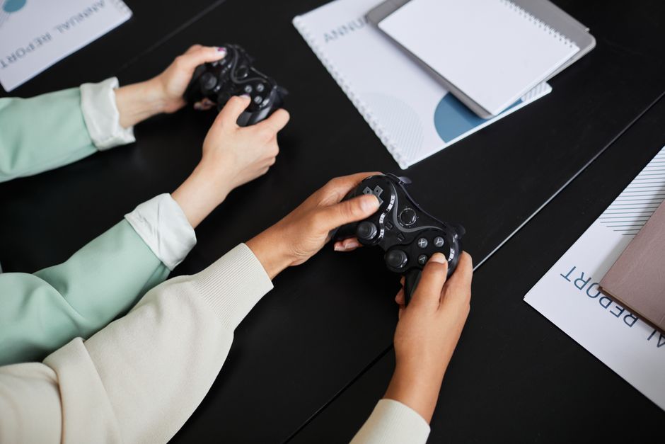 Close-up of three hands holding different console controllers, highlighting shared play during a small gathering.