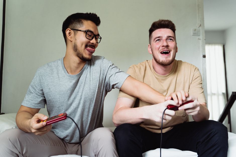 Three friends, two men and one woman, sitting together on a couch, all looking at a large TV screen and laughing, enjoying a cooperative PC game in a shared, positive environment.
