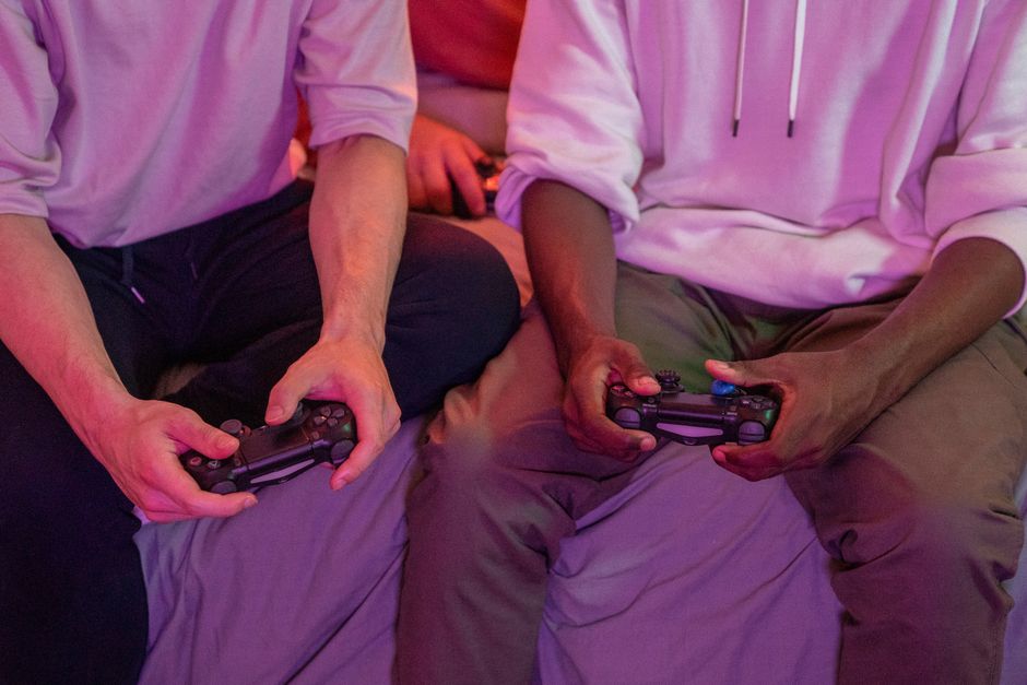 Four friends sitting on a couch, focused and cooperating while playing a video game on a large screen.