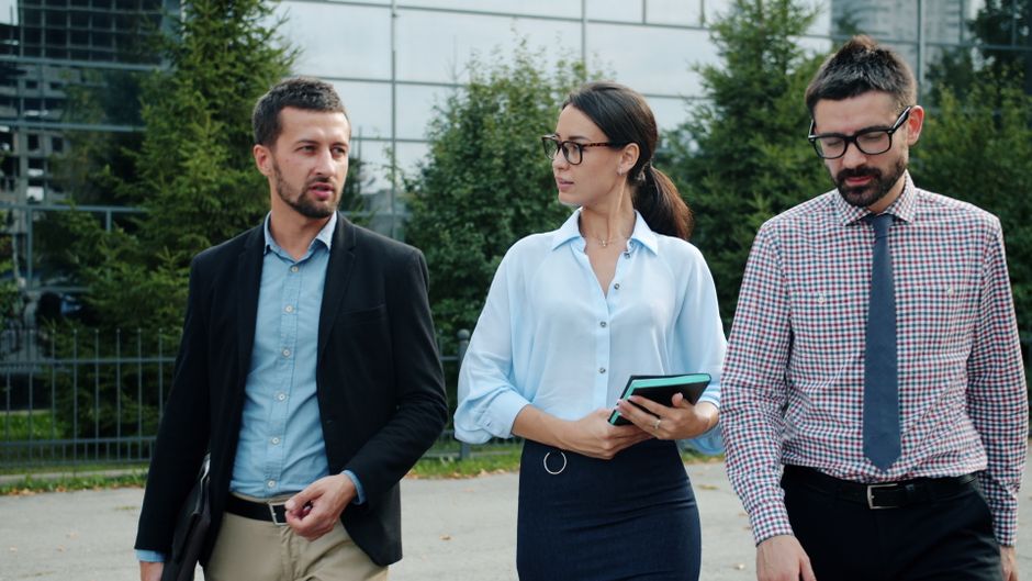 A small, diverse team walking together outdoors in a green space, casually conversing and gesturing, illustrating an effective in-person walking meeting environment.