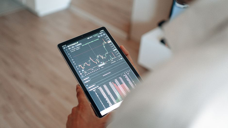 A hand holding a stylus interacts with a tablet displaying a colorful budget pie chart and transaction list, symbolizing AI-assisted money management.