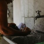 Traveler hand washing a t-shirt in a hotel sink with travel-sized detergent.