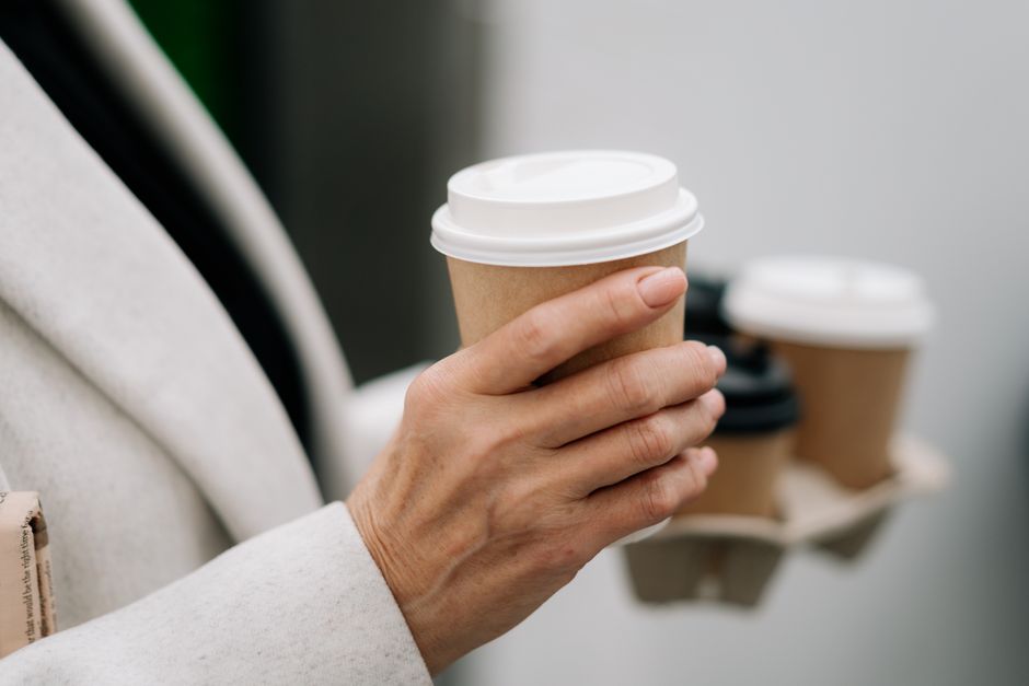 A set of three hands each holding a different coffee cup: one regular, one half-caf, and one decaf, illustrating choice in caffeine intake.